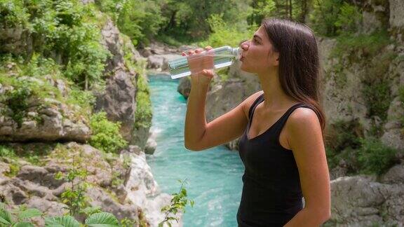 开朗的年轻女子在山间小溪边观景饮水
