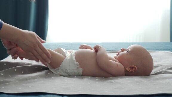 妈妈慢慢地抚摸着宝宝的身体按摩着宝宝新生的宝宝靠窗躺在床上