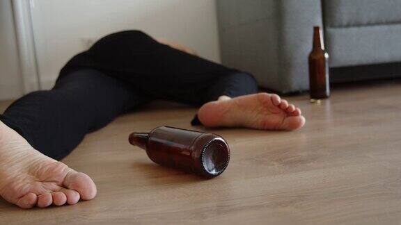 一个喝醉了的年轻人睡在家里的地板上旁边的地板上滚着一个啤酒瓶