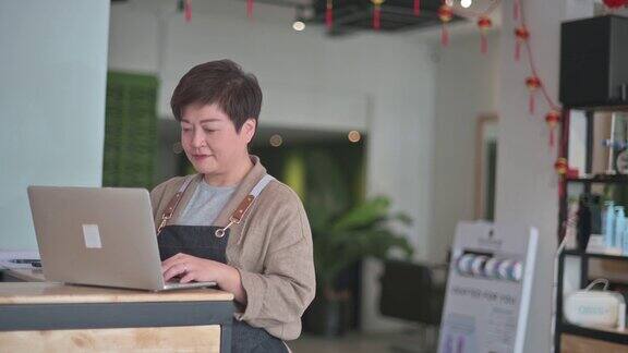 亚洲华人发廊女商人在柜台用笔记本电脑更新她的客户数据