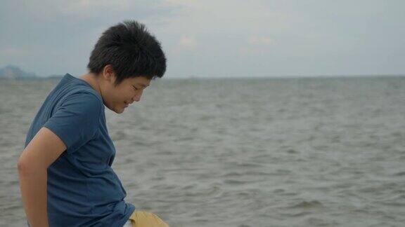 快乐的亚洲男孩坐在海边的岩石上在阳光明媚的日子里看海滩的景色生活理念