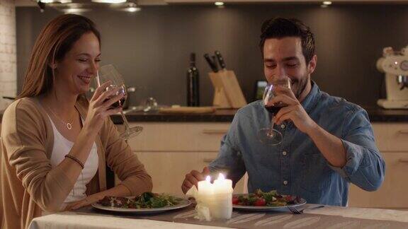 一对美丽的夫妇在厨房里吃烛光晚餐他们吃喝聊天庆祝时他们碰杯