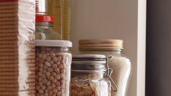 一个男人从食品储藏室的架子上取下或放置装满豆类的玻璃瓶