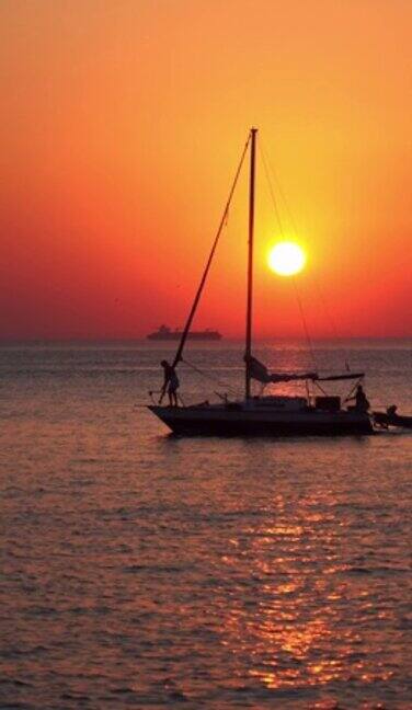 一艘小帆船在夕阳和橙色的天空前航行