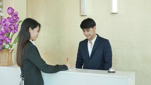 亚洲商务女性在大堂与酒店接待员签署房间预订表格