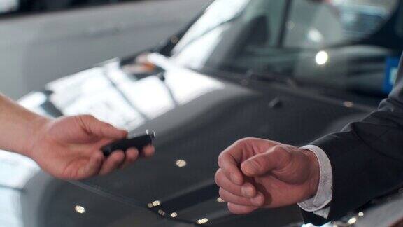 年轻人给买家汽车钥匙男人握手在美丽的汽车经销商的背景购买汽车