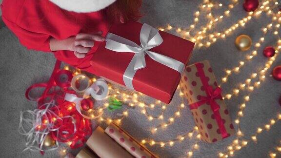 戴圣诞帽的女孩用红色包装纸制作新年包裹年轻女子正在为她的朋友和亲戚包装圣诞礼物装饰为冬季假期做准备