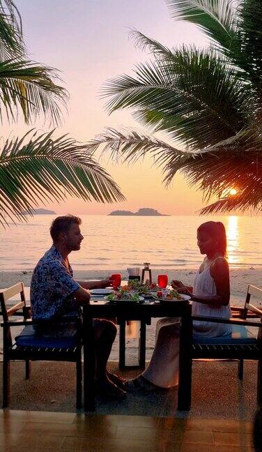 日落时分一对情侣在泰国昌岛的海滩上享受浪漫的晚餐