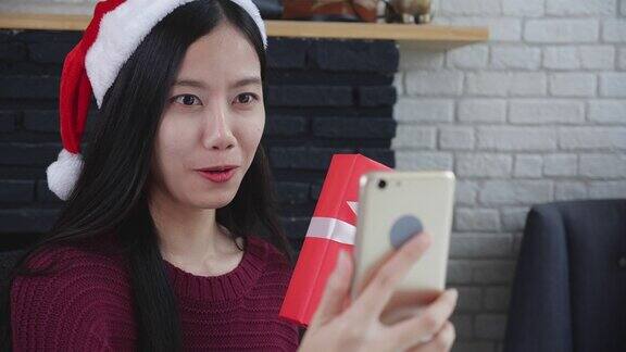 年轻的亚洲女性与朋友在线视频通话并在圣诞节在家电话上展示礼盒社交距离新常态女性视频会议沟通和节日概念