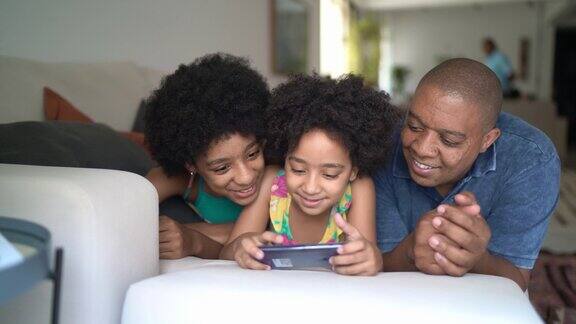 父亲和女儿一起躺在家里的沙发上使用智能手机