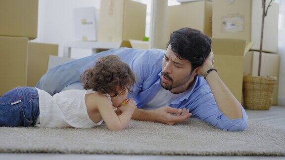 父亲和一头卷发的快乐小女婴躺在地板上父亲说话而他的女儿在吃咬苹果而准备搬进新家与纸板盒的背景