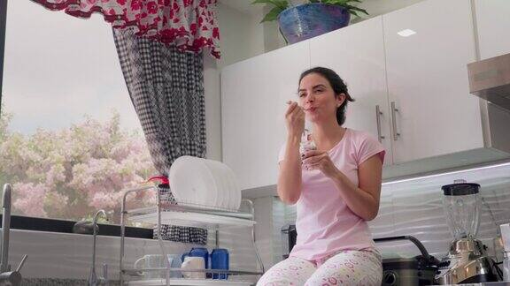 西班牙年轻女子坐在厨房柜台上吃酸奶的慢动作