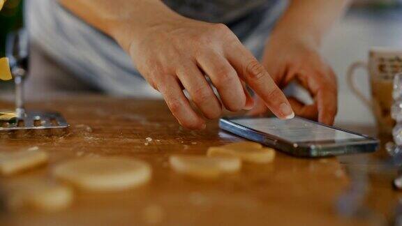 一个女人在厨房里用抹刀拿起生饼干用手机打电话