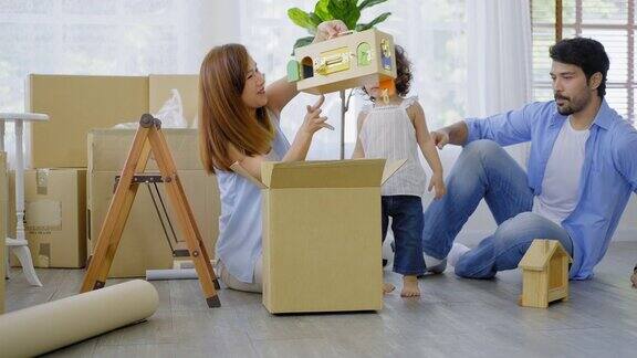 年轻的爸爸妈妈和可爱的小女孩打包和把玩具放进纸板箱一起准备搬进新家的背景有许多纸板箱