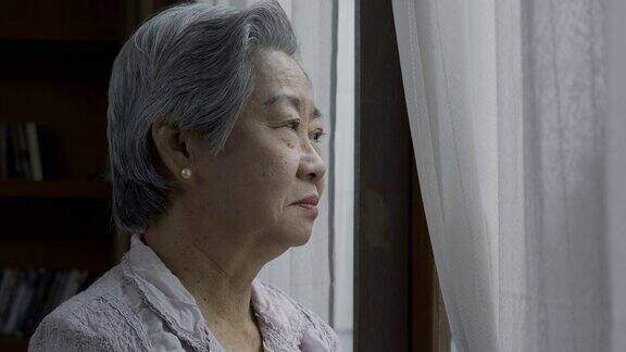 心烦意乱的老太太擦着眼泪独自在窗边哭泣孤独终老特写脸的悲伤的老女人与灰色的头发