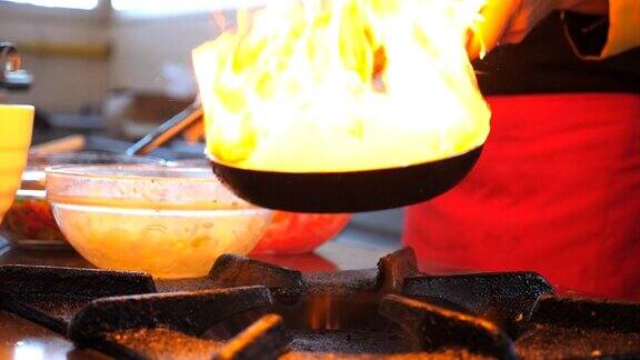 在酒店的厨房里不知名的厨师拿着两个平底锅煮着火焰风格的菜男厨师在炉子上的煎锅里翻炒和煎蔬菜烹饪慢镜头