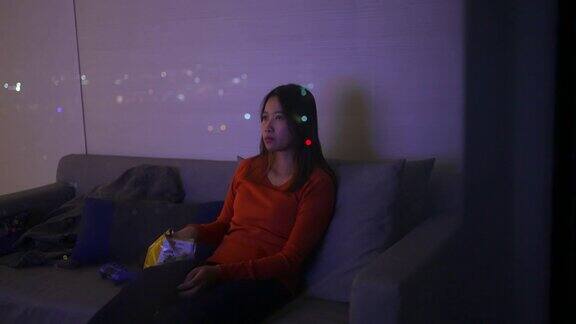 4K亚洲女人晚上坐在沙发上看电视吃着薯片