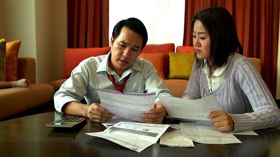 丈夫和他的妻子在计算他的账单而他的家人在沙发上财政问题很严重