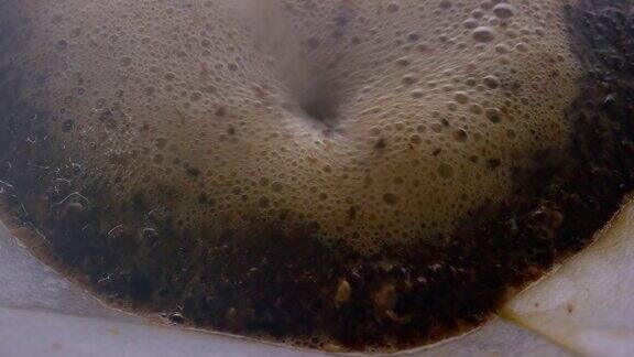 微距拍摄的热水倒在一个咖啡壶的纸过滤器上的新鲜咖啡渣
