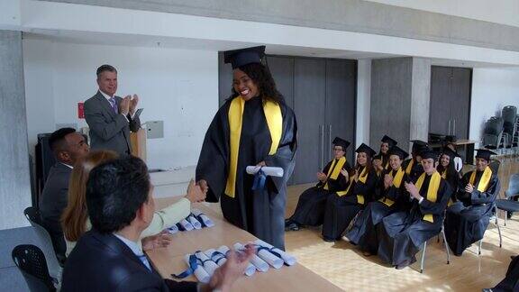 快乐的非裔美国女毕业生接受她的文凭并与老师和院长握手