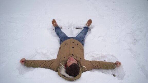 一个年轻人的肖像穿着夹克和牛仔裤躺在雪地里英俊的男人说谎摊开双手闭上眼睛在冬季公园的乐趣松软的雪包裹着周围的一切