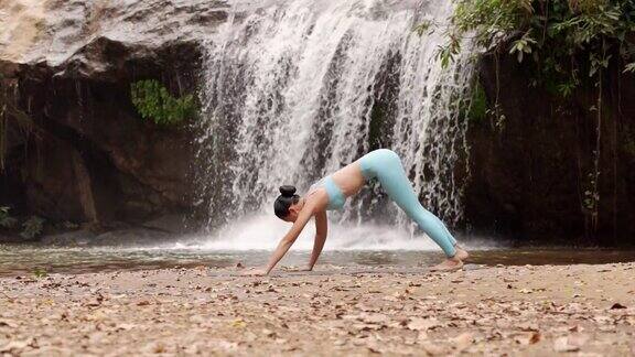 女人练习瑜伽在自然瀑布旁边