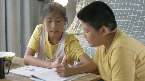 亚洲男孩教家庭作业给他的妹妹在家里男孩和女孩坐在靠近窗户的地板上与狗