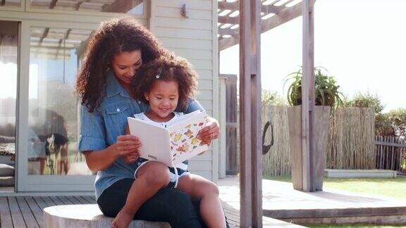 一个年轻的黑人女孩坐在户外妈妈的膝盖上看书