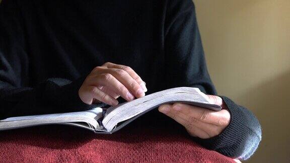 一个女人在桌子上读圣经手指一行一行地移动文本