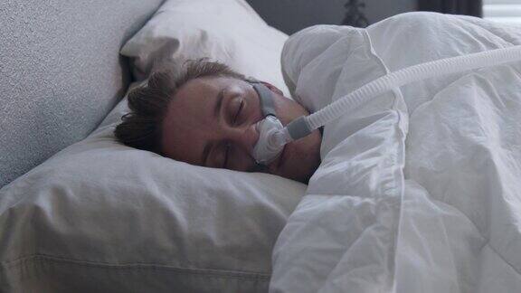 一个患有睡眠呼吸暂停的年轻人戴着CPAP口罩在床上侧睡