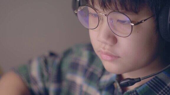 戴着眼镜的亚洲男孩坐在家里的一个房间里在线学习