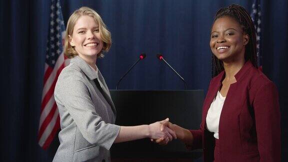 在蓝色的美国国旗背景下两位女政治家在镜头前握手