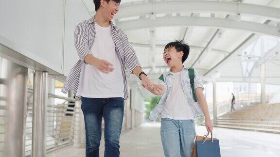 年轻的亚洲男孩拿着五颜六色的购物袋和父亲一起走在购物中心购物的乐趣年终礼物的快乐年中促销和假日概念