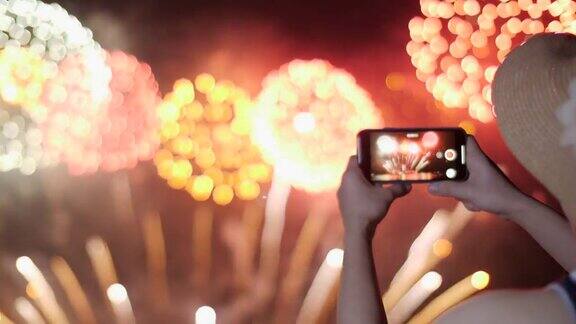 一名女子用手机拍烟花剪影背景上的天空照亮了烟花
