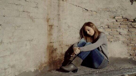 一个悲伤沮丧的女人独自坐在一堵旧墙旁