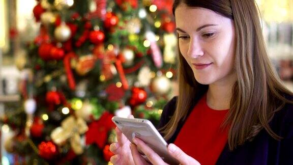 女人靠近装饰过的圣诞树漂亮的女性用手机收到新年祝福
