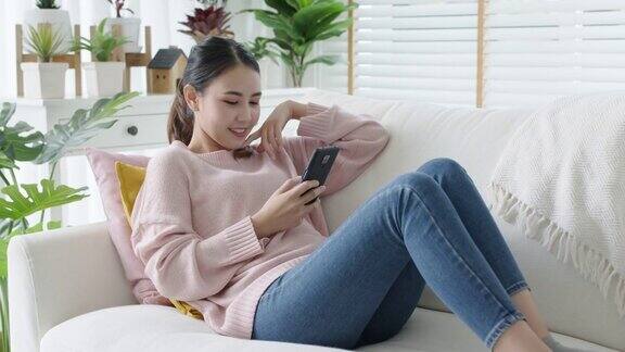 年轻迷人美丽随意的亚洲女性在沙发上看手机玩社交媒体