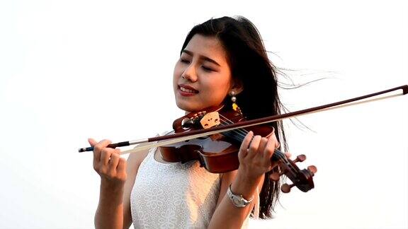 年轻美丽的亚洲女孩穿着裙子站在海滩上拉小提琴
