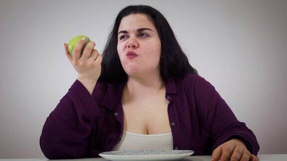 年轻丰满的白人妇女拿着苹果签名的肖像烦恼胖女孩吃健康食品肥胖、医疗保健、生活方式