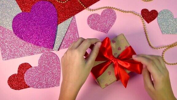 包装情人节或生日礼物情人节礼物用红纸做的心形放在木桌上前视图粉红色的背景