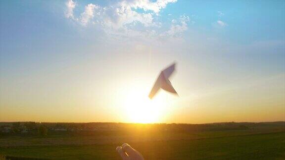在夕阳的背景下手将纸飞机放飞到天空