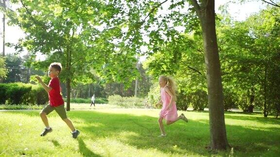 三个活泼的孩子在阳光明媚的夏日公园的草地上奔跑慢动作跟踪拍摄
