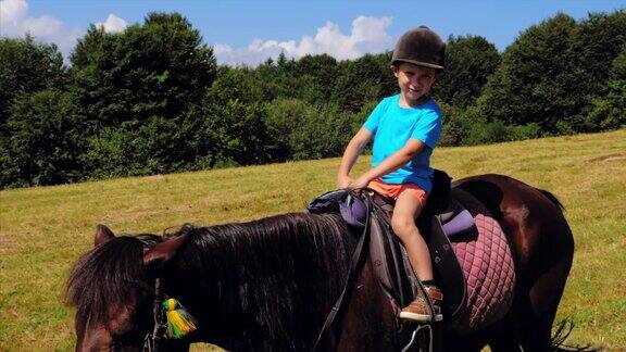 快乐的男孩戴着头盔骑着棕色的马在山上