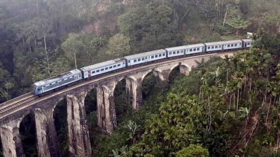 无人机拍摄到斯里兰卡埃拉丛林中著名的蓝色火车经过一座古老的九拱桥