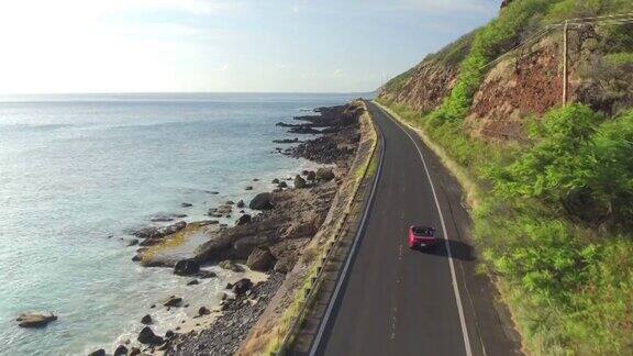 一辆红色敞篷车在岩石海岸上的海岸公路上行驶