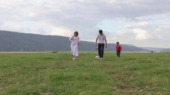 暑假亚洲家庭在河边的草地上踢足球