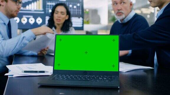会议室笔记本电脑在会议桌上绿色键盘屏幕在后台商务人士有重要的讨论