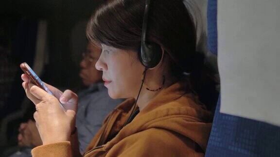 亚洲女性在飞机上用智能手机选择和听音乐