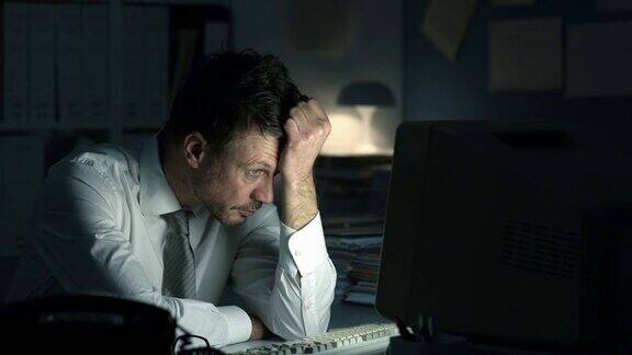 一位疲惫沮丧的商业主管在办公室工作到深夜他坐在办公桌前盯着电脑屏幕等待