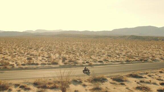 日落时分男子骑摩托车沿着沙漠公路的鸟瞰图